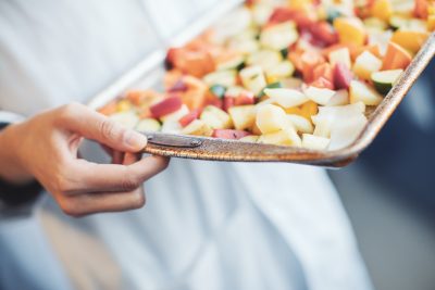 A student holds a pan of chopped vegetables and potatoes.