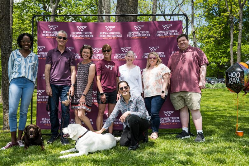 A group of Virginia Tech HNFE faculty, staff, and students as well as two dogs stand outside during a department event for a group photo.