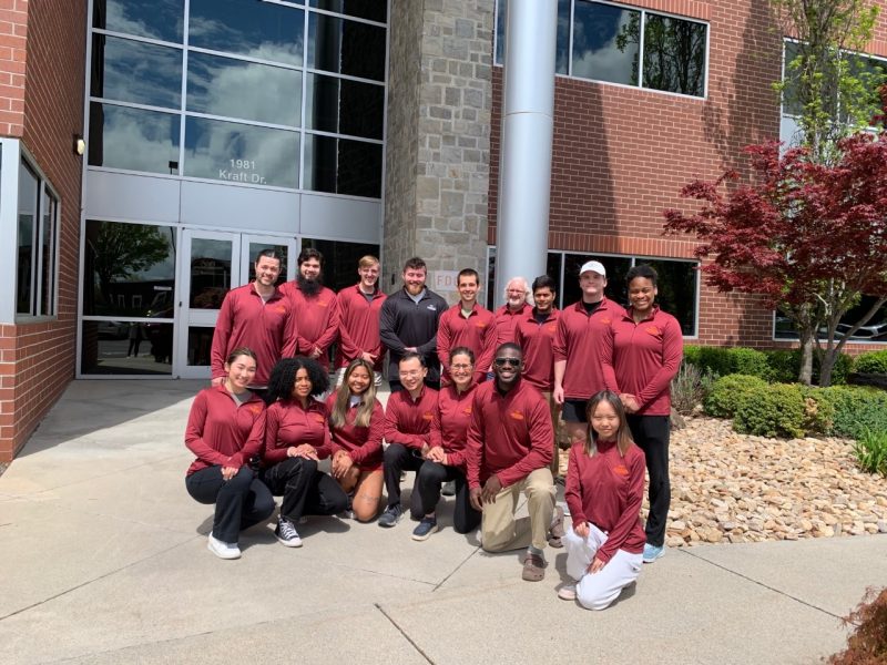 A group of undergraduate and graduate researchers stand in a group photo with their faculty advisors outside.