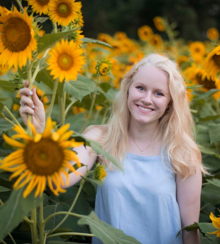 A Virginia Tech HNFE Ambassador stands among a field of sunflowers and smiles for a photo.