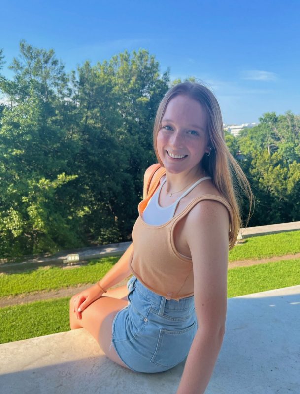 A Virginia Tech HNFE Ambassador sits on a sidewalk and looks over her shoulder to smile for a photo.