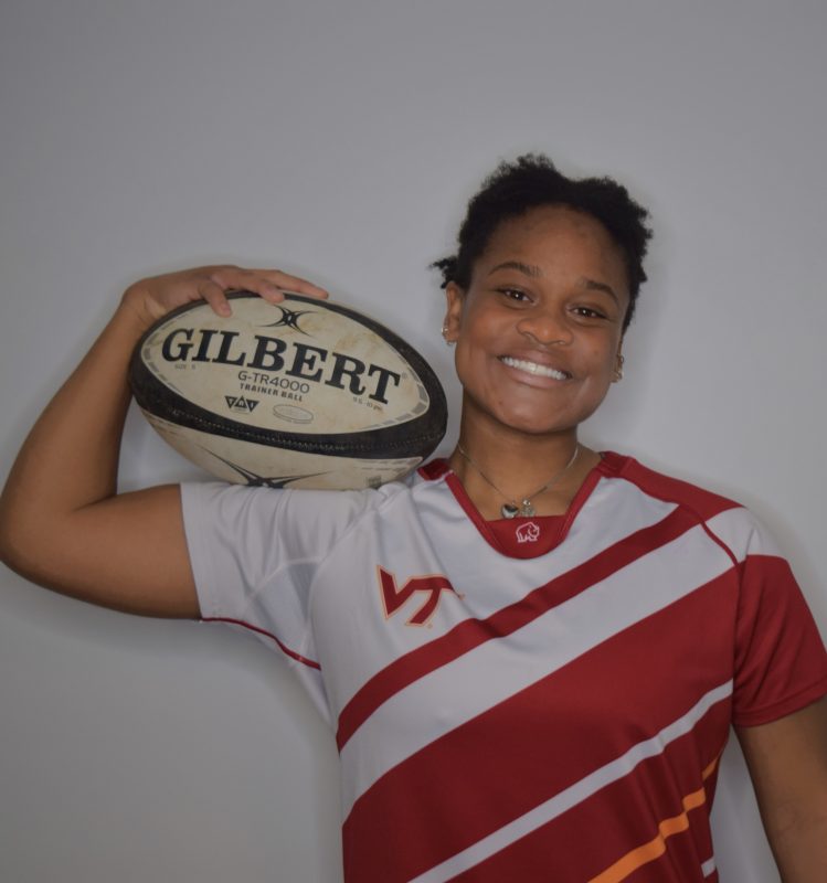 A Virginia Tech HNFE Ambassador poses against a wall holding a football.