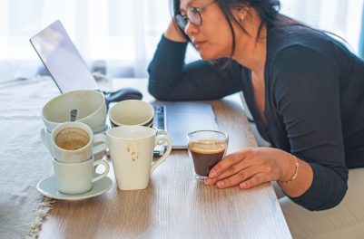 person at computer surrounded by cups of coffee